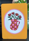 A decorative card or print with rounded corners, featuring a yellow-orange border and a central illustration of a pink checkerboard pitcher filled with dark red flowers and green leaves, set against a softly blurred indoor background with flowers.